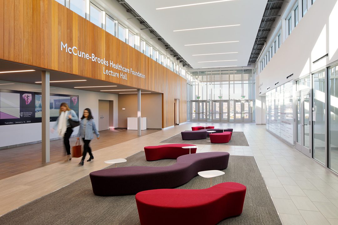 Image of an interior lobby with lots of natural daylight, soft seating, and a wooden wall with signage that says "McCune-Brooks Healthcare Foundation Lecture Hall"