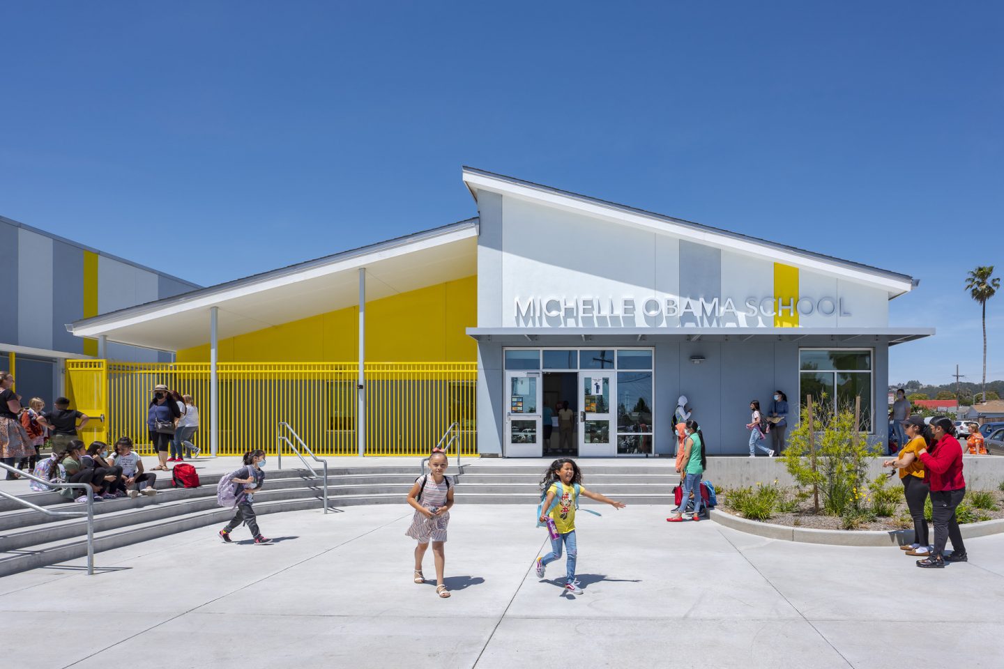 Image of the front entry of Michelle Obama School with elementary students and parents/guardians