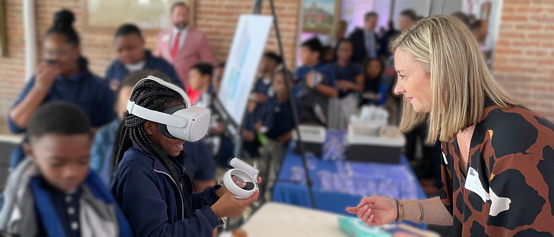 Image showing Multistudio's Lexi Tengco helping a little girl use virtual reality goggles to view the proposed design for the Lemann Building renovation.