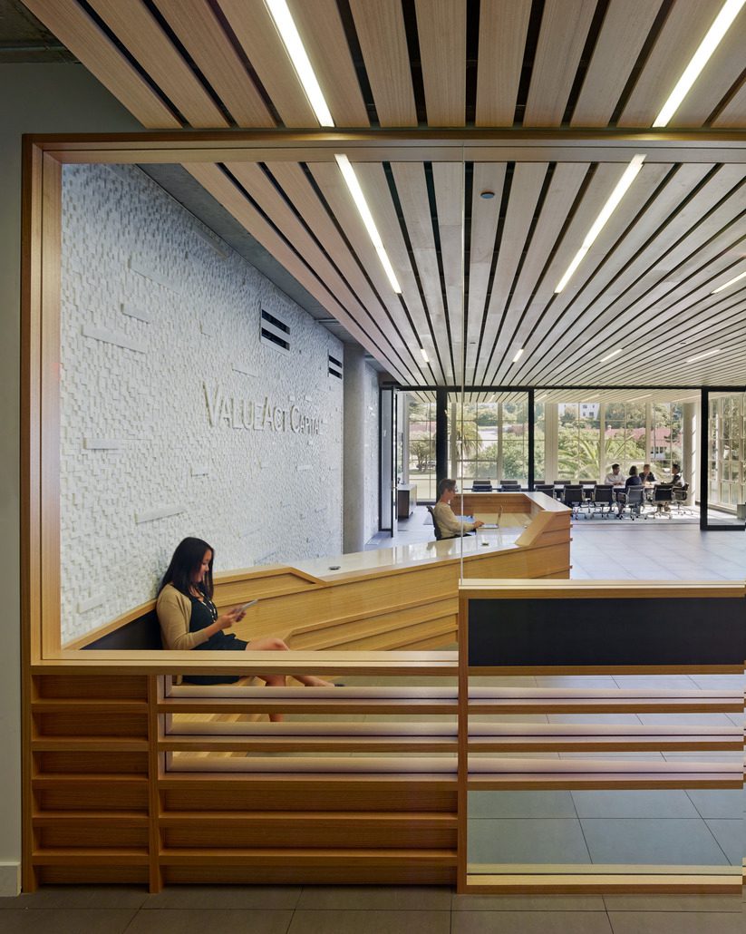 Image of the main entry and reception area for ValueAct Capital highlighting a ribbon wall of board and batten eucalyptus that starts at the reception desk and bends to form a bench and wraps around the glazed main entry..
