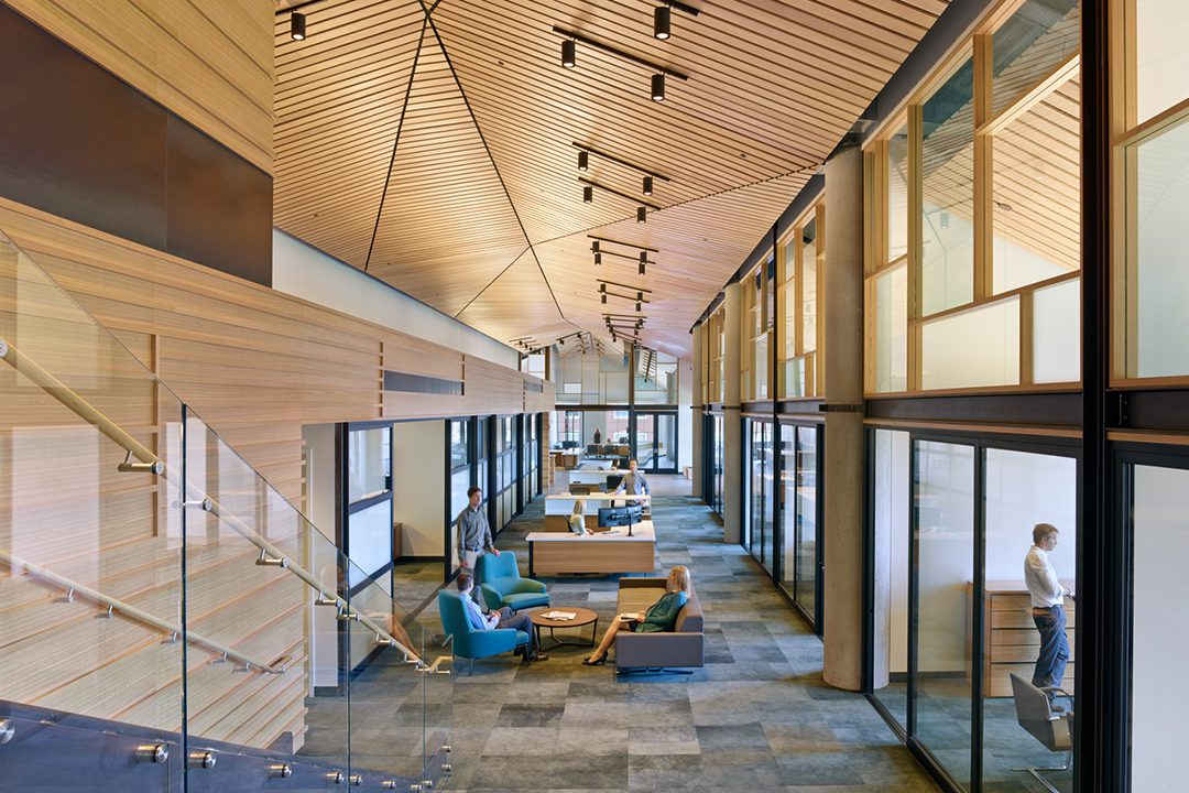 Image of the ValueAct Capital offices with woman sitting on a couch in the foreground with other employees positioned throughout the space. The eucalyptus used for the ceiling and walls creates a warmth throughout the space.