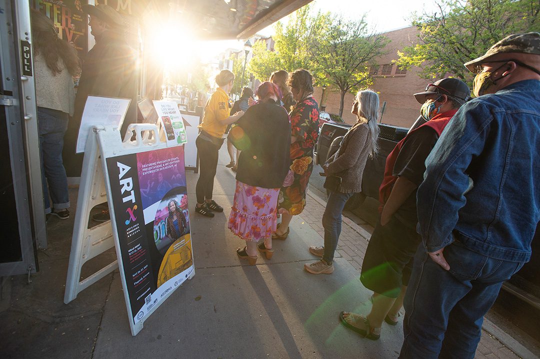 Photo of A-frame sign in front of people lining up to attend an ARTx event.