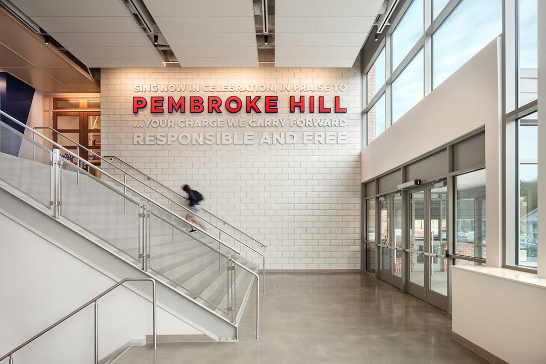 Photo of interior entry of the Bellis Athletics Center with graphic signage that says "Sing now in celebration, in praise to Pembroke Hill... your charge we carry forward responsible and free."